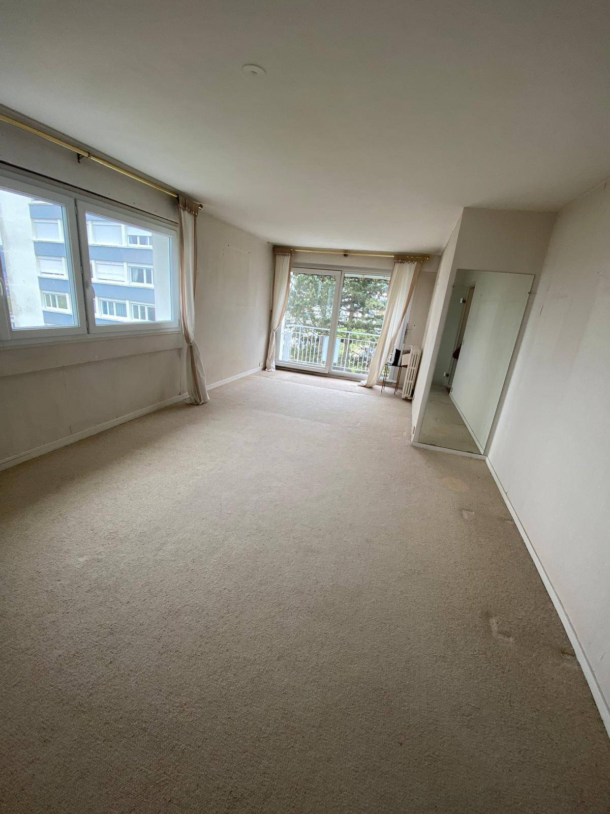 Pièce de vie vide avec moquette beige avant rénovation